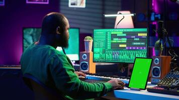 Young musician mixing and mastering songs next to isolated mockup display, operating on digital audio software to add sound effects on new tracks recorded. Audio engineer in home studio. Camera A. video