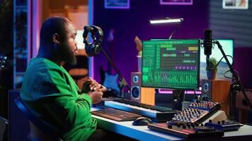 African american sound engineer using midi controller notes to add audio effects in post production, editing tracks with digital software and mixing console. Male musician in home studio. Camera A. video