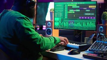 Musician playing piano keys and editing to improve sound quality of audio recordings in his home studio, putting on headset. Music producer uses midi controller to manipulate sounds. Camera A. video