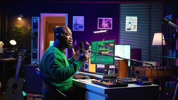 Male composer recording his melody on microphone in home studio, singing a song of his own creation. Talented artist using audio files and lyrics to apply mixing and mastering techniques. Camera B. video
