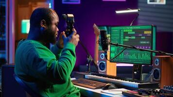 Artist composer recording a new track on his home studio microphone, editing his song with professional gear. Adjusting volume levels and adding sound effects, mix and master. Camera A. video