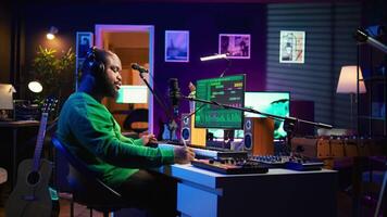 Professional artist writes new verses for a song in home studio, producing new music with mixing console and pc software. Composer works with audio equipment and tools, recording tunes. Camera B. video