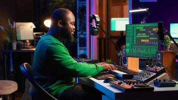 Audio engineer recording and producing new tunes on professional pc software, using mixing console and midi controller to create new music. Artist composer uses stereo gear at home studio. Camera A. video