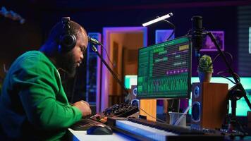 Music technician with headset mixing and mastering his audio recordings, operating on console in home studio. Musician producer creating new tunes with sound effects in post production. Camera B. video