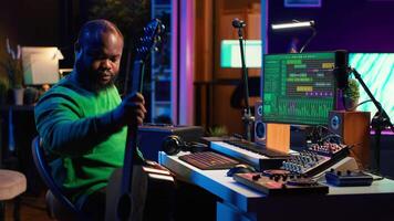 Musical producer prepares to record tunes on acoustic instrument, working in personal home studio to record soundtrack. Sound composer recording guitar music, editing with mixing console. Camera A. video
