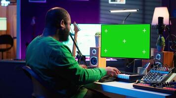 Artist plays midi controller synthesizer next to green screen layout, working on producing new music with his audio musical instruments in home studio. Musician using isolated copy space. Camera A. video