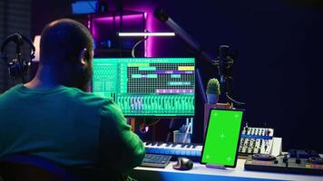 Songwriter composer mixing and mastering tracks next to green screen, operating on digital audio pc interface to add sound effects on new recordings. Technician in home studio. Camera B. video