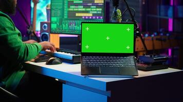 Producer editing his audio files and recordings on digital pc interface, sitting next to an isolated mockup screen. Sound engineer mixing and mastering songs with console in home studio. Camera A. video
