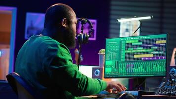 Producer composing new track with electronic gear in his home studio, creating music on mixing console and software interface. Talented artist songwriter controls panel to produce sounds. Camera A. video