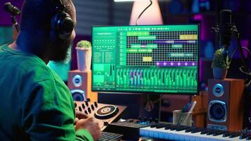 Young musician twisting knobs and mixing tunes with a console, following record settings on a digital software interface. Artist composer producing new music hits in his home studio. Camera A. video