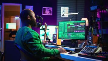 African american artist composing a new soundtrack for a project, using professional production software in home studio. Skilled creative singer producing music and adding sound effects. Camera B. video