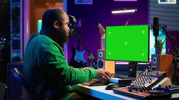 Songwriter operates on synthesizer piano keys next to isolated display, composing new music with instruments and stereo tools in home studio. Artist producer works with green screen. Camera B. video
