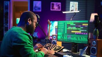 Skilled male composer producing new songs on his mixing console, operating on professional gear in home studio. Artist audio engineer twisting knobs to adjust sound levels on tracks. Camera B. video