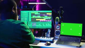 Music producer mixing and mastering songs on digital post production pc interface, green screen display. Artist adding sound effects and adjusting volume levels to produce new music. Camera B. video