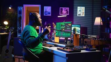 Confident songwriter performing a tune on microphone in home studio, recording his song and editing in post production. Performer artist singing aloud and using stereo equipment. Camera B. video