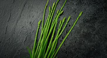 Fresh Asparagus Stalks With Water Droplets on Black Slate Surface photo
