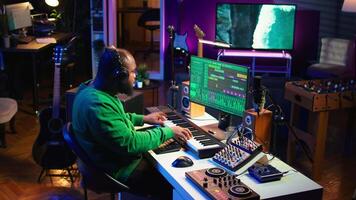 Musician playing piano keys and editing to improve sound quality of audio recordings in his home studio, putting on headset. Music producer uses midi controller to manipulate sounds. Camera B. video