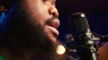 Artist records his voice on microphone in home studio singing a song composed by him. Skilled musician using recordings and lyrics to edit in post production, mixing and mastering session. Camera A. video