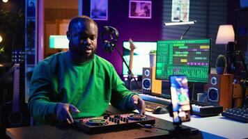 Skilled audio engineer teaching online mixing tunes lessons by using smartphone on tripod to record himself in home studio. Producer hosting a master class with soundboard console gear. Camera B. video