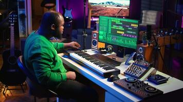Sound engineer recording piano notes with DAW software in his home studio, working at night on producing new music with electronic tools. Musician composing tunes on midi controller. Camera B. video