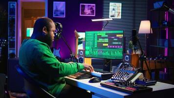 Songwriter mixing and mastering tracks on stereo console, playing electronic keyboard in home studio. Artist oversees audio performances to create melody, producing tunes with piano keys. Camera B. video