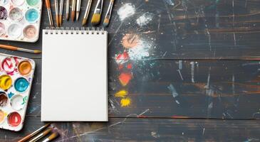 Art Supplies on a Wooden Table With Blank Sketchbook and Used Paint Palette photo