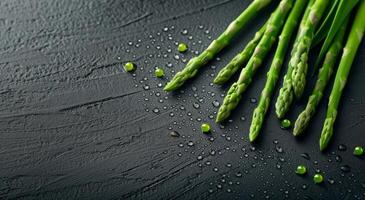 Fresh Asparagus Stalks With Water Droplets on Black Slate Surface photo