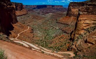 Dirt road at the bottom of the canyon among the layered geological formations of red rocks. photo