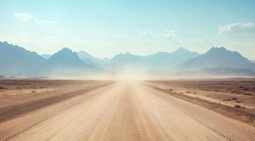 A gravel road stretches endlessly into the horizon, surrounded by majestic mountains amid a vast and dry desert landscape. Dust particles dance playfully in the warm air beneath a clear blue sky photo