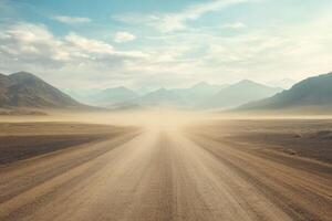An endless, deserted gravel road stretches out boldly into the vast horizon, surrounded by an expansive, arid landscape that features rugged mountains and a beautiful cloudy sky overhead photo