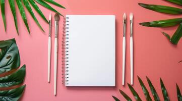 This sophisticated mockup features a pristine notepad alongside artistic brushes and vibrant tropical leaves, perfect for creative projects that require both style and inspiration photo