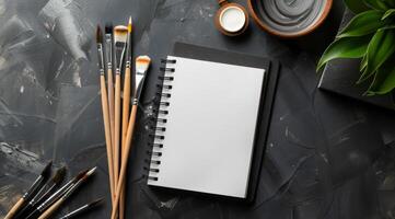This stylish mockup features a blank notebook, colorful paint brushes, and a vibrant green plant, ideal for showcasing artistic projects and inspiring creativity through visual representation photo