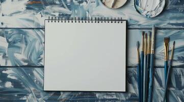 An open sketchbook rests on a textured blue surface, paired with brushes and vibrant paint, creating an ideal setting for artists to unleash their creativity and bring visions to life photo