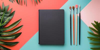This vibrant workspace mockup features a sleek black notebook with colorful paintbrushes and lush greenery, creating an ideal setting for artistic inspiration in crafting and design photo
