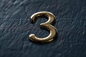 A detailed closeup of a shiny gold number three resting on a dark, textured surface that is ideal for design projects photo