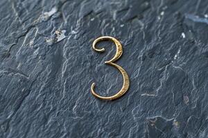 An elegant gold numeral 3 is showcased on a textured slate surface, perfect for various design projects photo