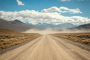 A long, deserted gravel road stretches endlessly into the shimmering horizon, beautifully framed by an arid, desolate landscape with distant mountains rising under a wide and clear blue sky photo