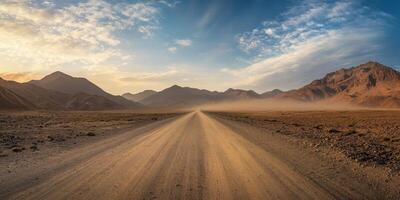 A lonely gravel road stretches endlessly into the horizon amidst a vast, barren landscape, bordered by majestic mountains and illuminated by a stunning, vibrant sunset sky that captivates the senses photo