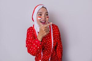 A hijab-wearing woman in a red outfit polkadot and an Indonesian flag headband poses in a celebration of Independence Day. The photo reflects patriotism and national pride.