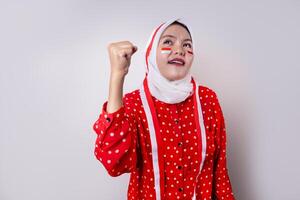 A hijab-wearing woman in a red outfit polkadot and an Indonesian flag headband poses in a celebration of Independence Day. The photo reflects patriotism and national pride.