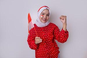 A hijab-wearing woman in a red outfit polkadot and an Indonesian flag headband poses in a celebration of Independence Day. The photo reflects patriotism and national pride.