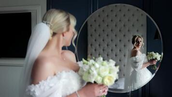 Bride admiring her reflection in a mirror, A beautiful shot of a bride holding a bouquet of white flowers as she admires her reflection in a large, round mirror. video