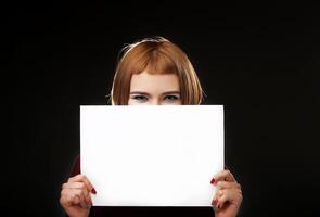 Red-haired woman holding an empty A4 card. Isolated on black background. Space for text photo