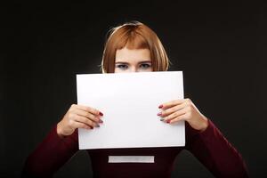 Young woman showing on empty blank board. Colorful studio portrait, isolated on black background. Space for text photo