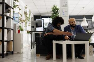 Two arab entrepreneurs reviewing financial analytics on laptop in unicorn business office. Executive manager and employee analyzing project progress in corporate coworking space photo