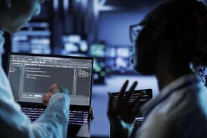 Trained programmers build firewall systems in server room housing advanced infrastructure. Skilled professionals run code on tablet and laptop, to upgrade data center rigs handling demanding workloads photo