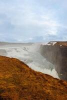 Large water flowing from hillsides and slopes in Iceland arctic Gulfoss cascade. Fabulous icelandic landscape with freezing river in nordic region falling off of cliffs, natural wilderness. photo