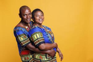 Smiling husband hugging wife from back while posing for portrait on studio orange background. Happy man and woman couple embracing and showing love while looking at camera photo