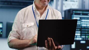 Aged developer expertly managing data while navigating in industrial server hub. Older programmer ensuring ideal cybersecurity protection, optimizing systems, close up photo