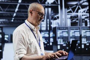 Elderly skilled IT developer in data center providing dedicated VPN servers able to deliver enhanced privacy, encrypted sensitive data, online anonymity and safe internet connections to users photo